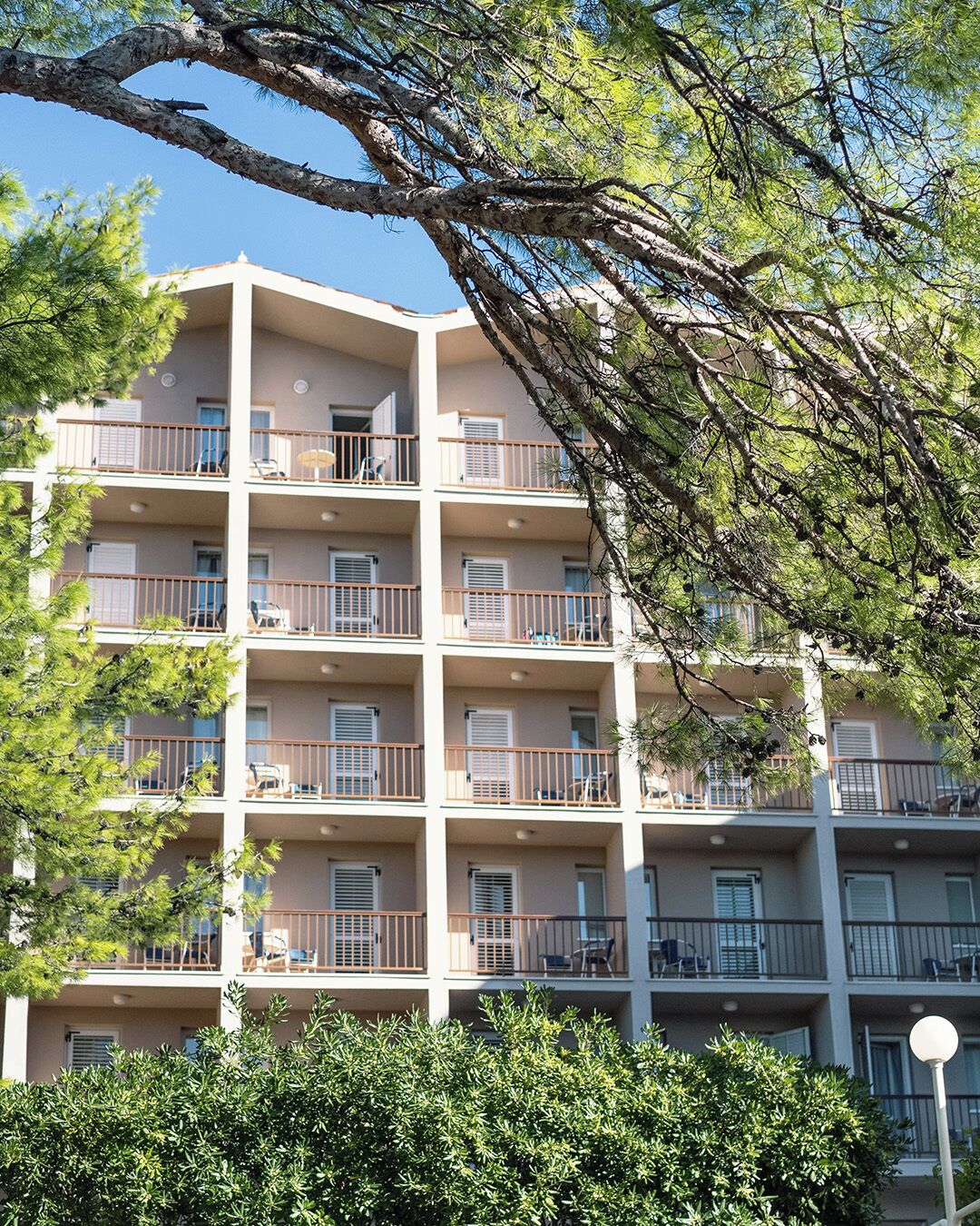 A multi-story residential building with balconies, surrounded by trees and greenery.