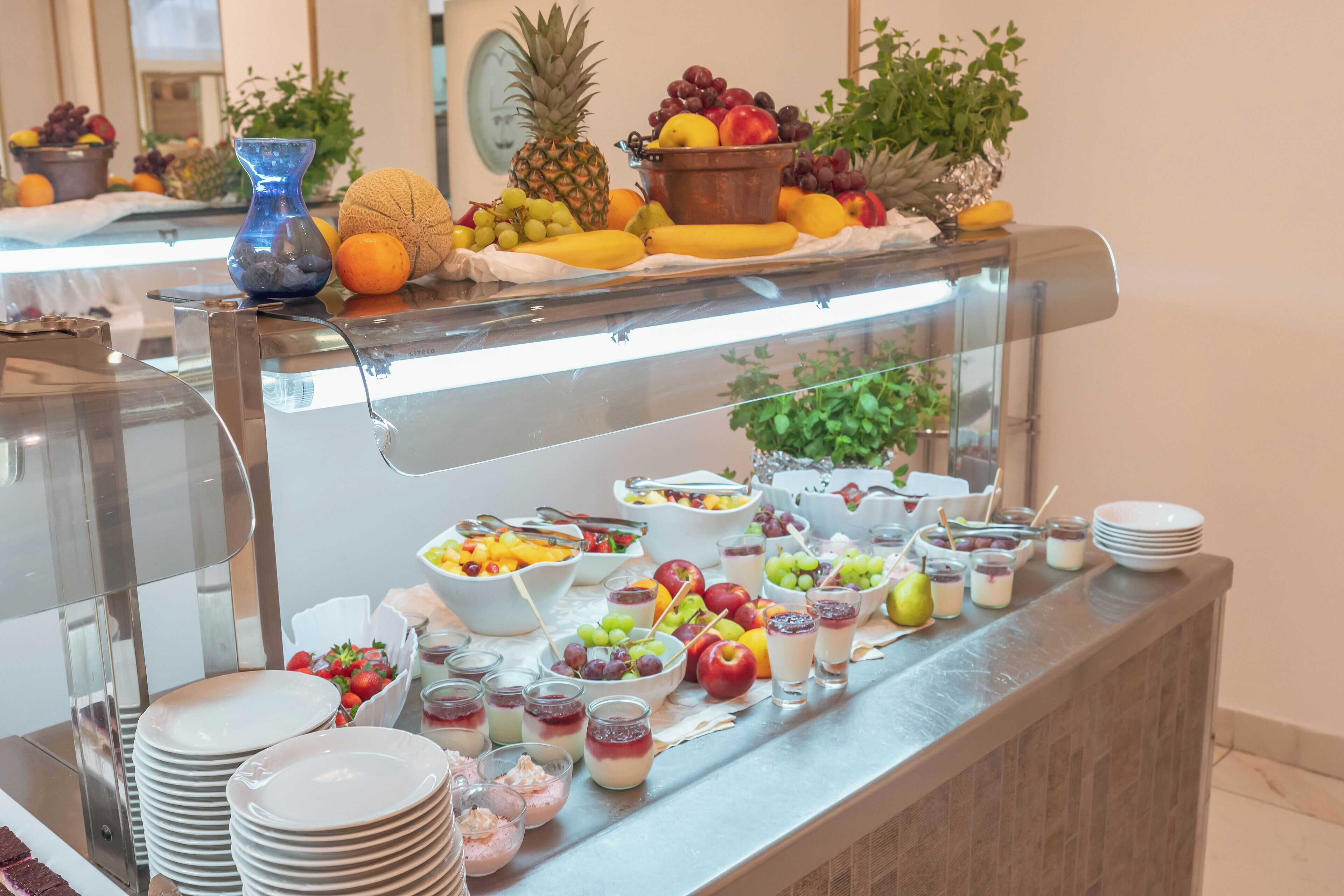 Un bufé con frutas variadas, fuentes de comida y platos apilados.