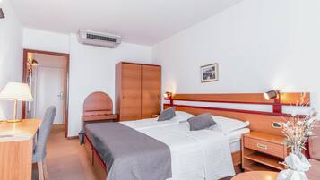 A hotel room with a bed, bedside table, lamp, chair, wardrobe, and an air conditioning unit.