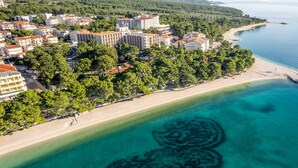 Luftaufnahme einer Küstenlandschaft mit Strand, Gebäuden und einer deutlichen Unterwasserformation.