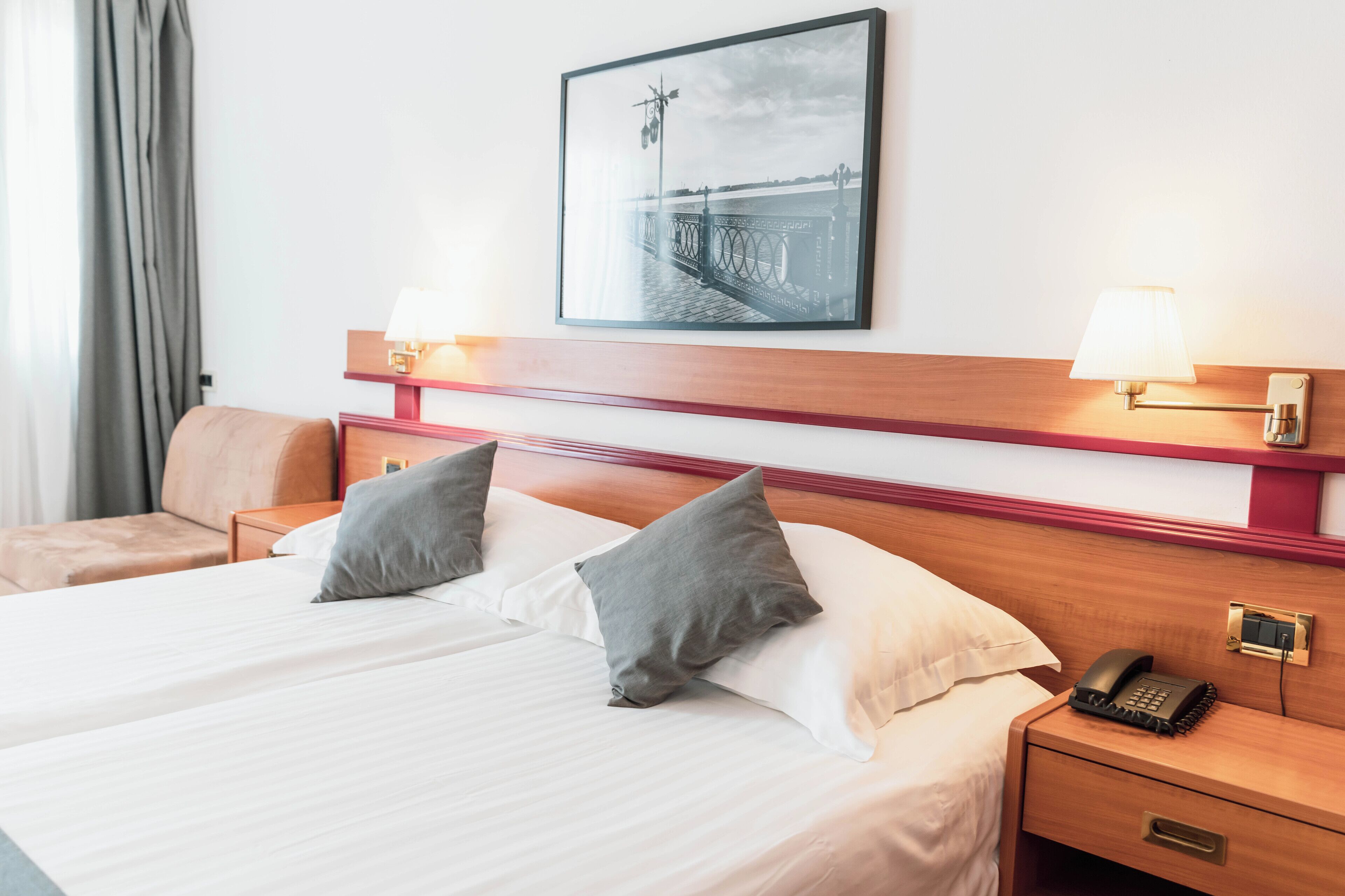 Habitación de hotel con una cama grande, dos mesitas de noche, una mesita auxiliar, un cuadro enmarcado en la pared y una lámpara en cada mesita de noche.