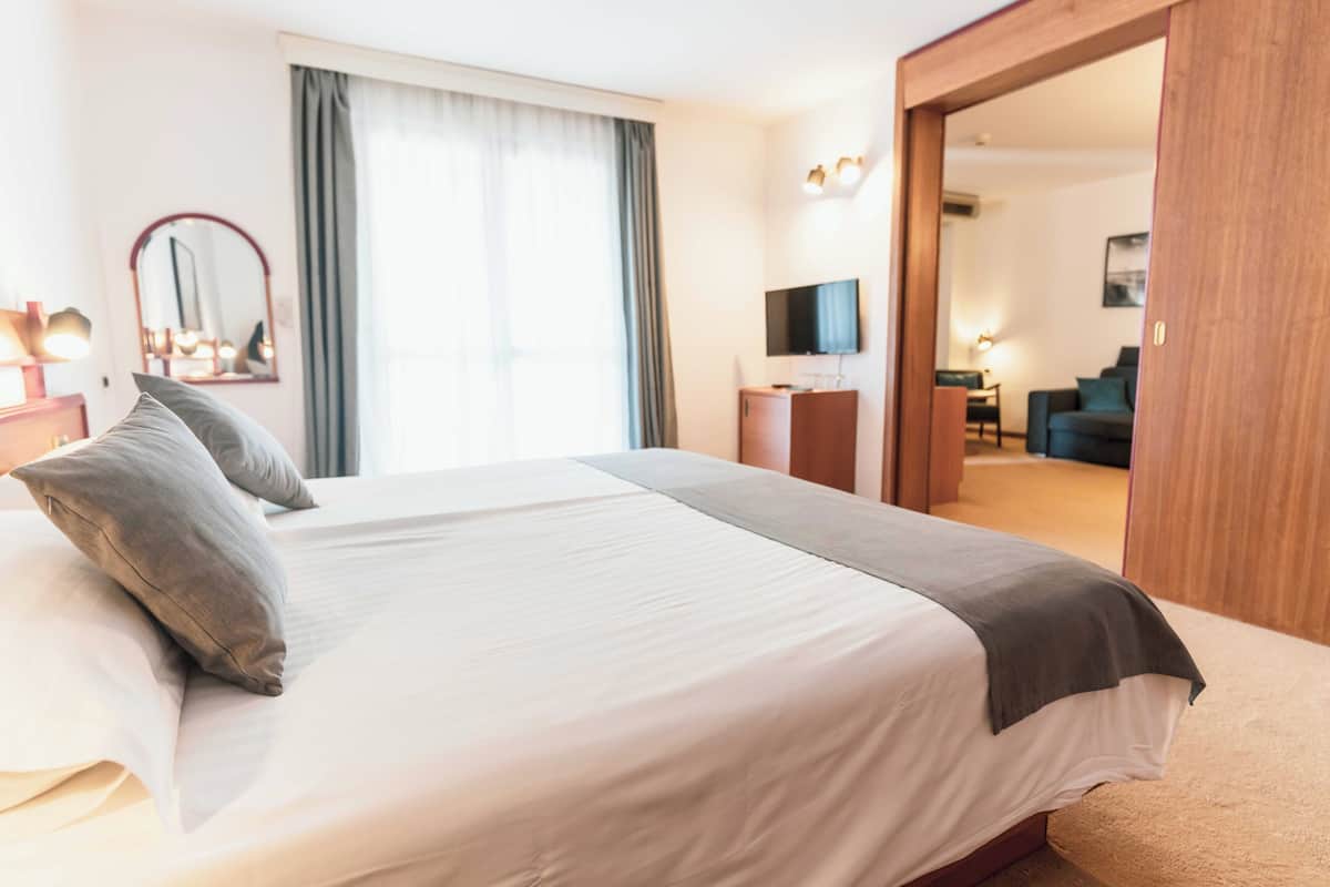 A hotel room with a large bed, a television, a mirror, and a view into the living area.