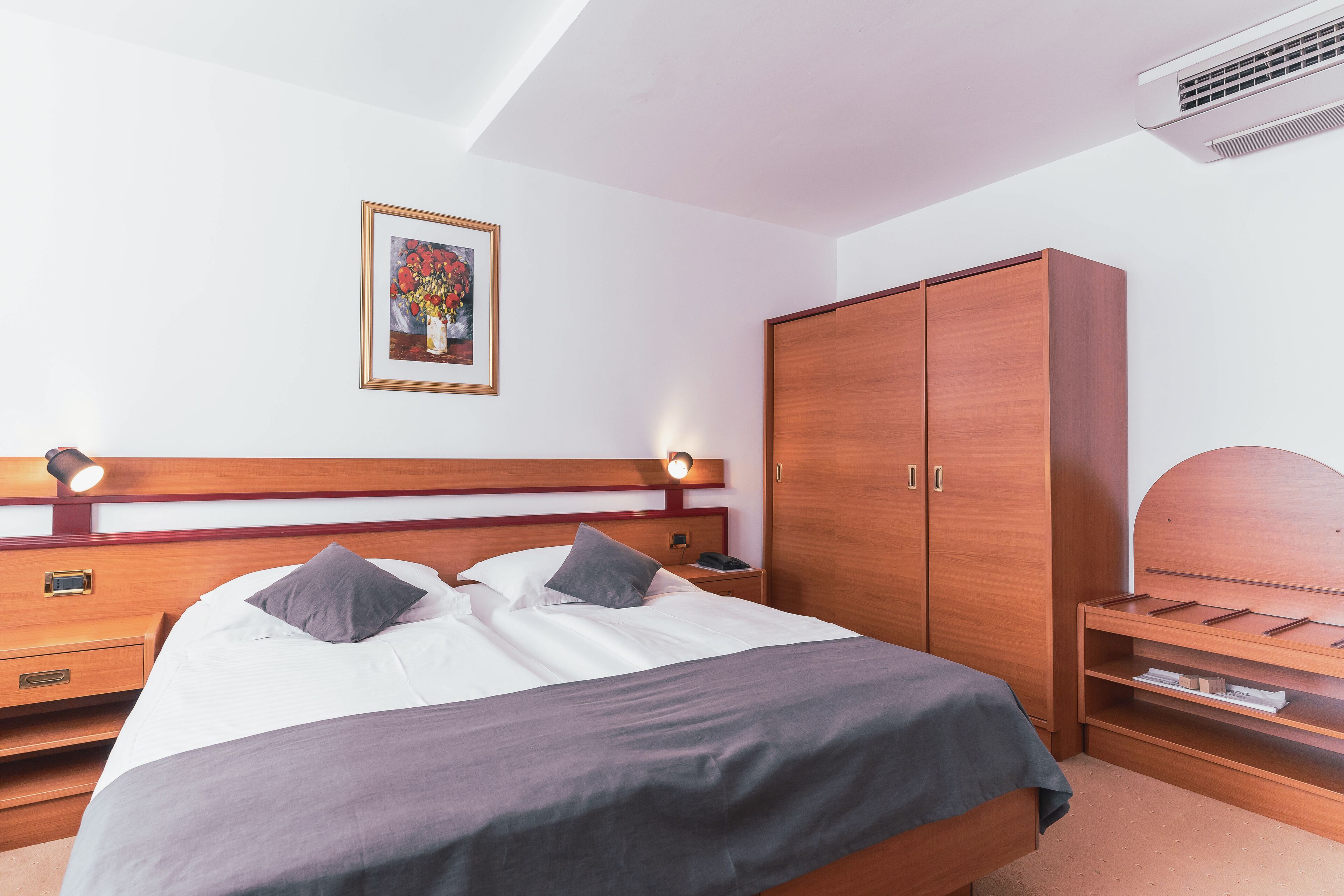 A neatly arranged hotel room with a bed, bedside tables, a wardrobe, and a framed picture on the wall.