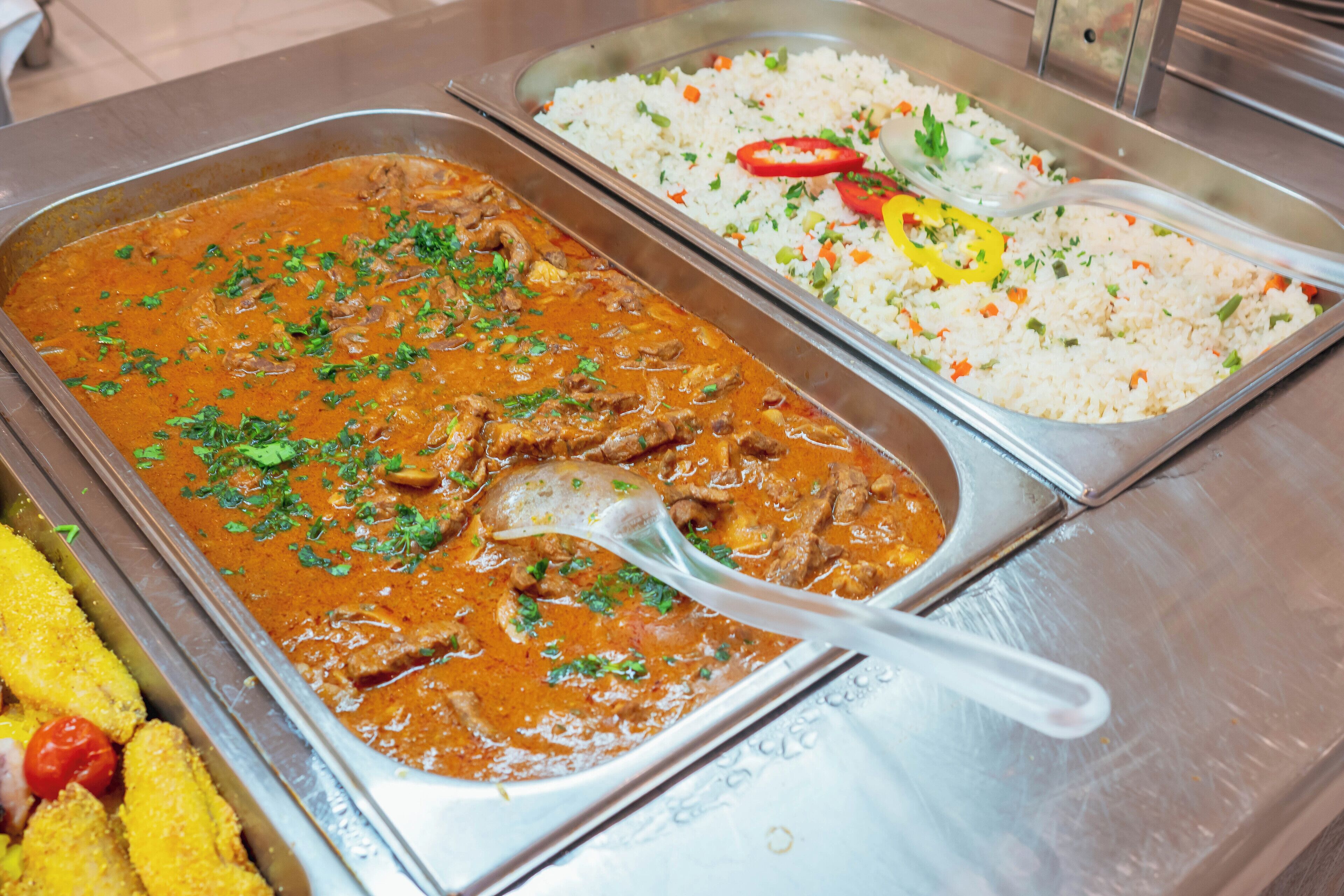 A buffet with a variety of dishes including a meat curry, rice with vegetables, and fried items.