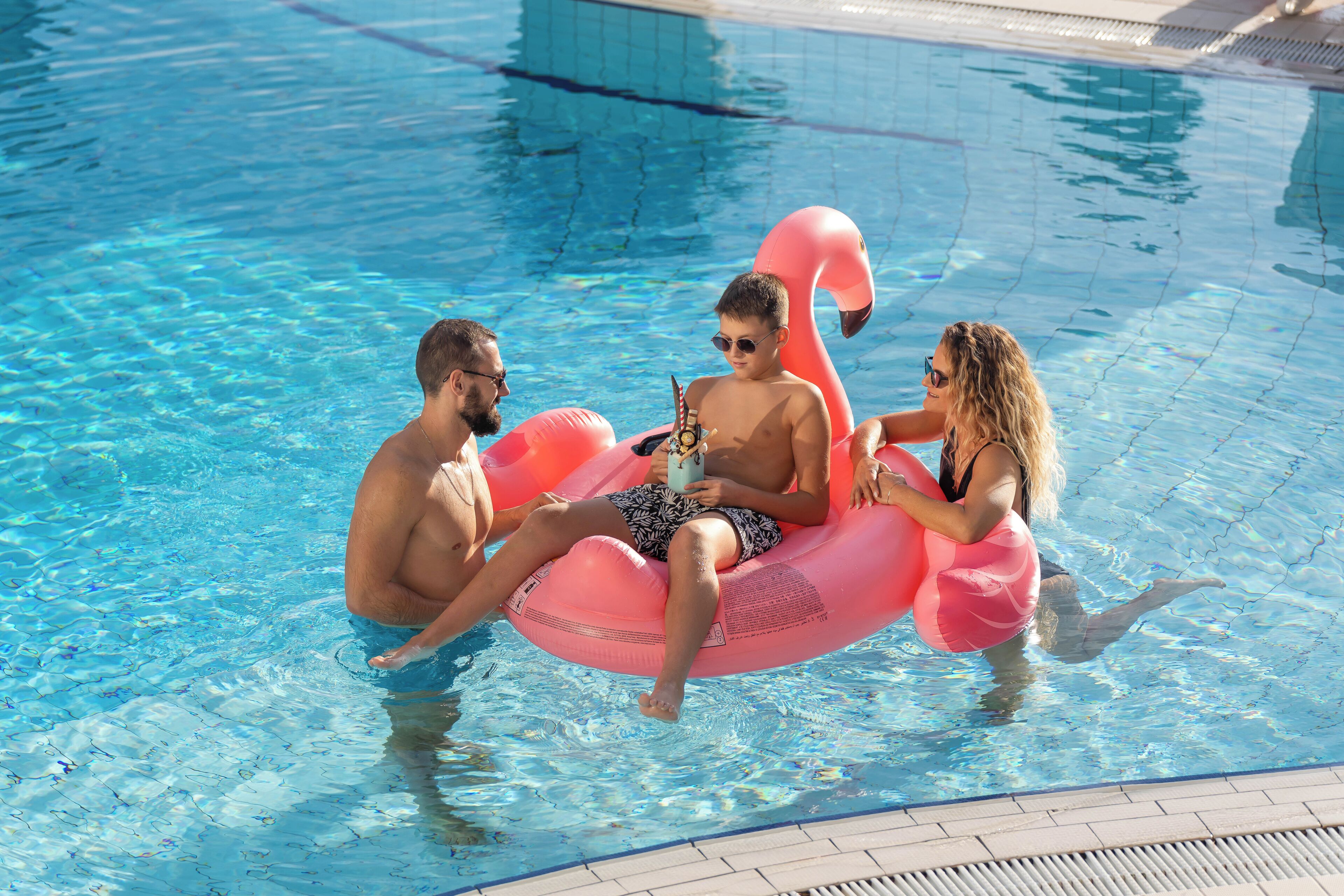 Tres personas en una piscina con un flotador con forma de flamenco rosa.