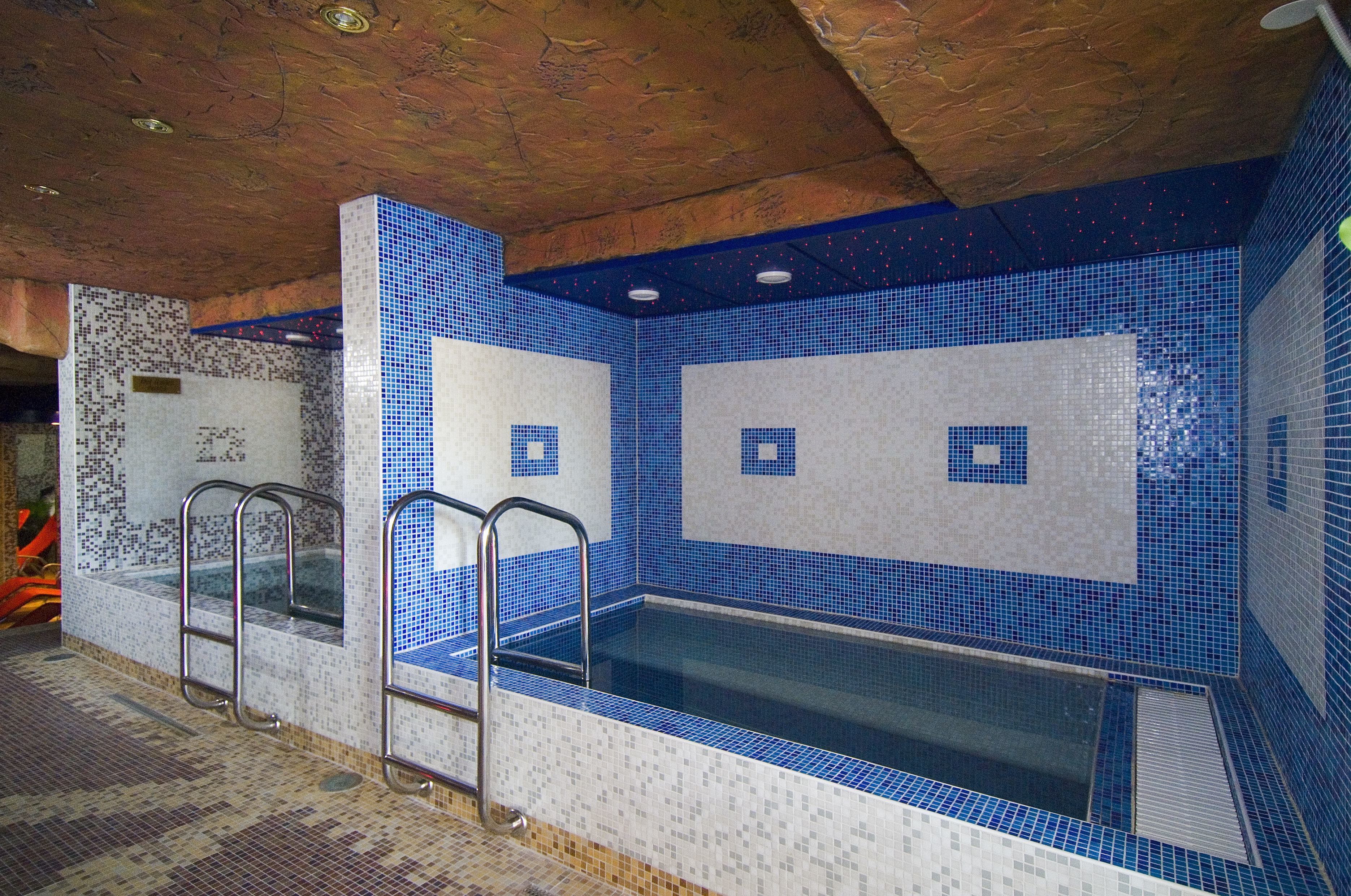 Una piscina con mosaicos azules, escaleras metálicas y suelo de baldosas.