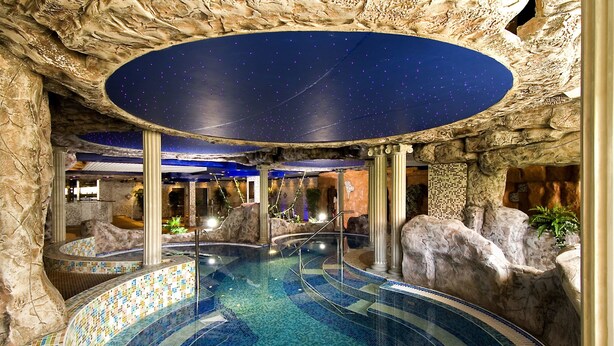 Ein Hallenbad mit Sternenhimmel, umgeben von Felsformationen und Säulen.