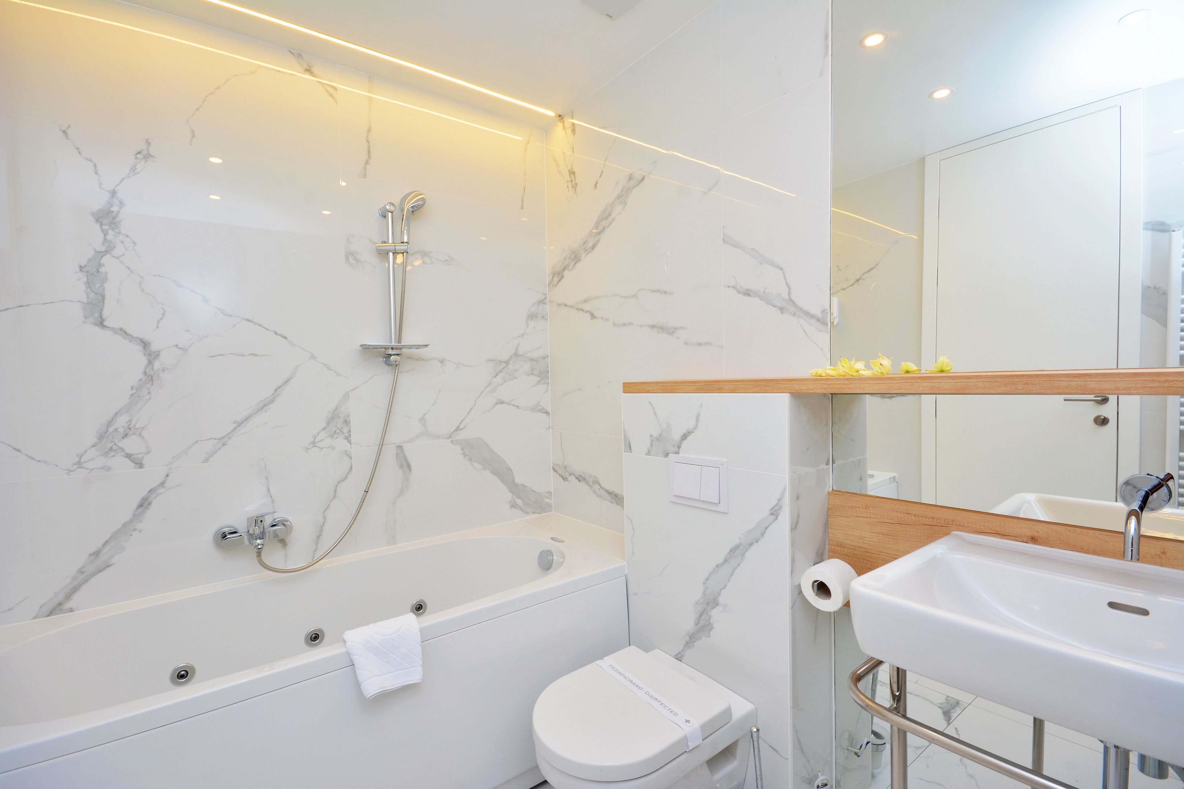 Un baño moderno con pared de mármol, una bañera, un inodoro y un lavamanos.