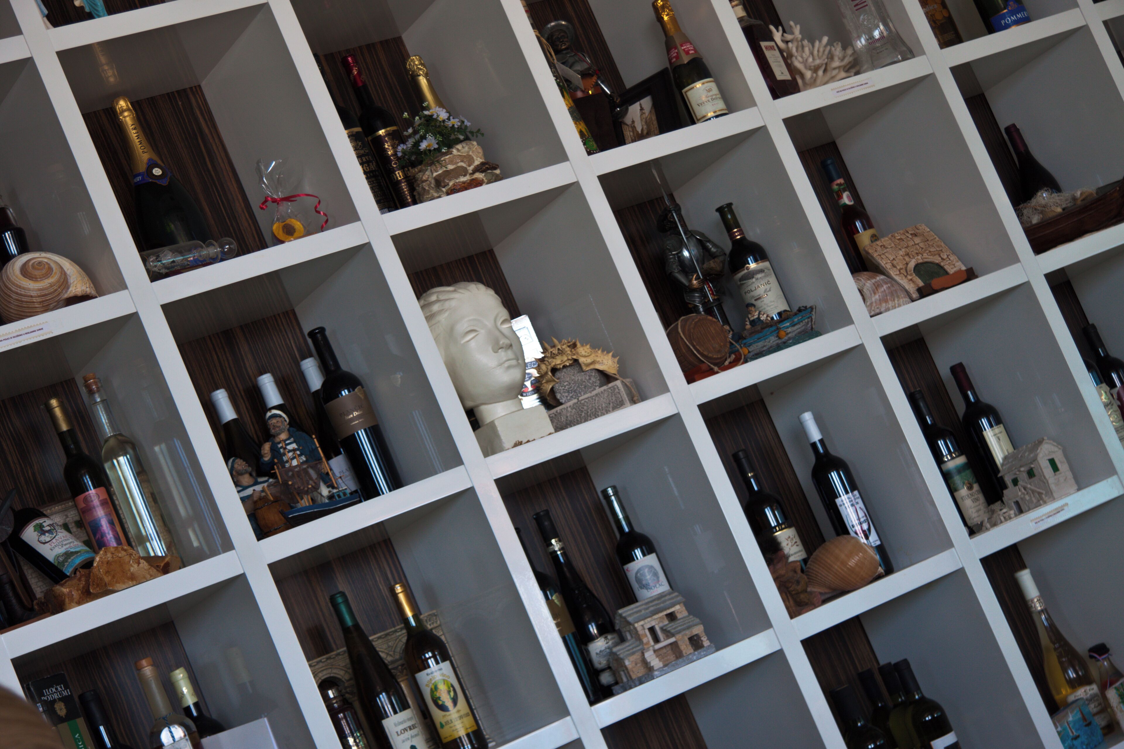 A wine rack with multiple shelves holding various bottles and decorative items.