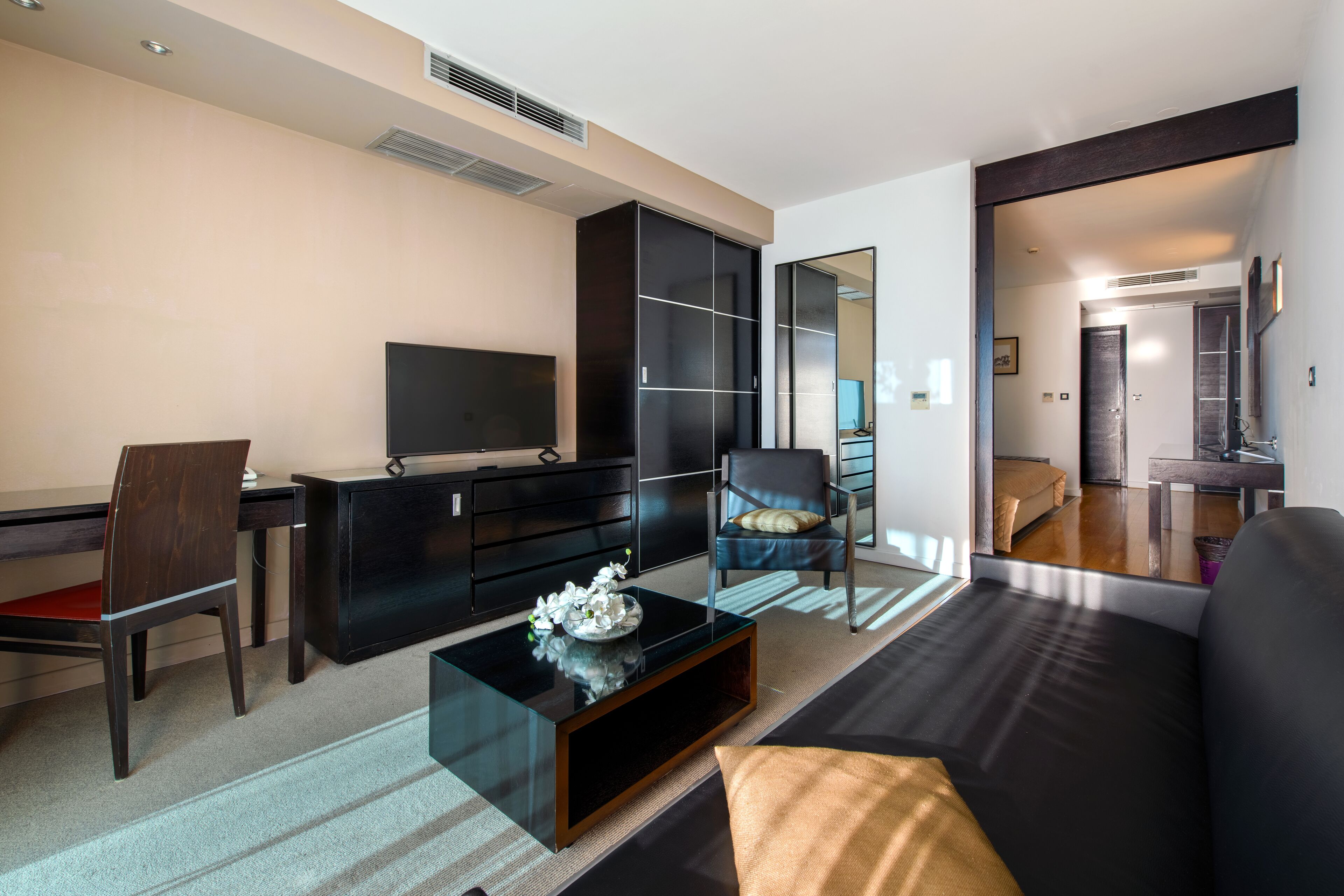 Una sala de estar moderna con un sofá negro, una mesa de centro de vidrio, un mueble negro para televisor, un armario negro y una pared espejada.