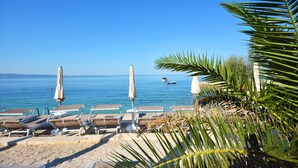 A beach with sun loungers and umbrellas, a clear blue sea, and a boat in the distance.