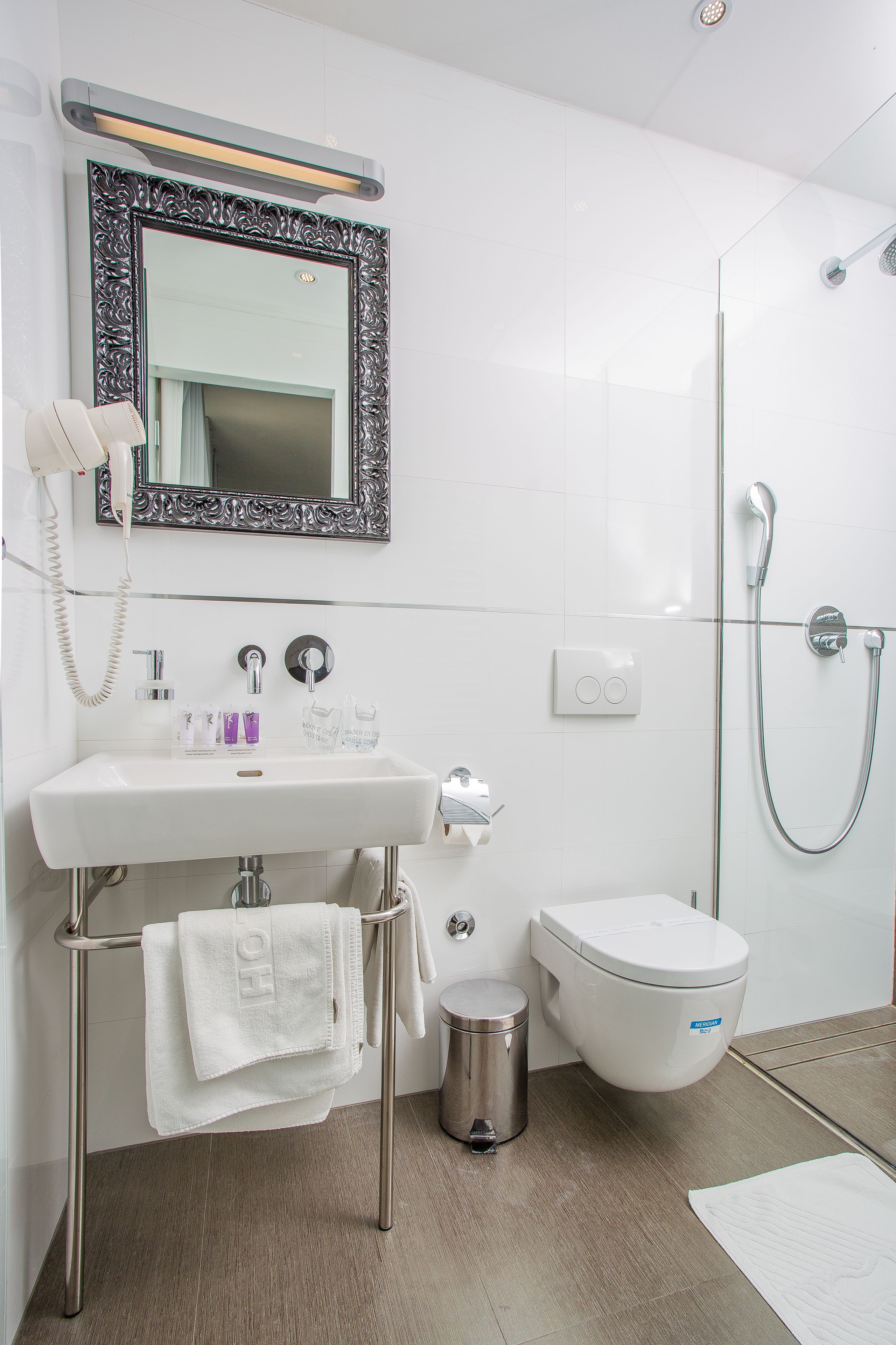 A modern bathroom with a white sink, a toilet, a shower, and a mirror with an ornate frame.