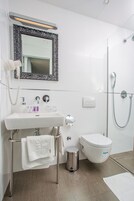 Um banheiro moderno com pia branca, vaso sanitário, chuveiro e espelho com moldura decorada.