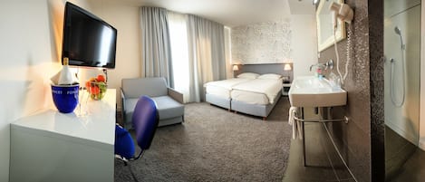 Une chambre d’hôtel comprenant un lit, un bureau avec une télévision, une chaise, et une salle de bain avec un lavabo et une douche.