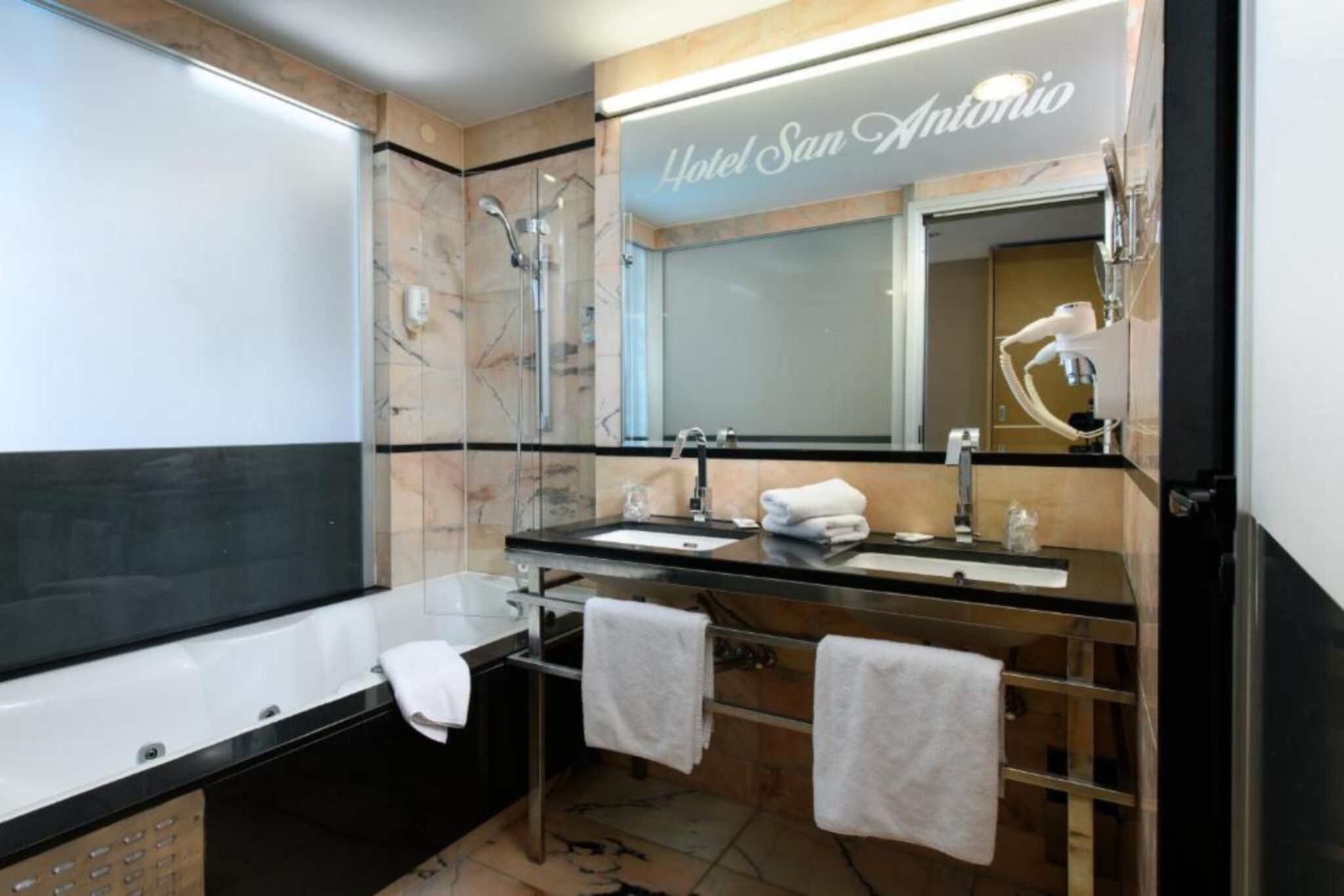 Un baño moderno con un espejo grande, dos lavamanos, una ducha y un perchero para toallas.