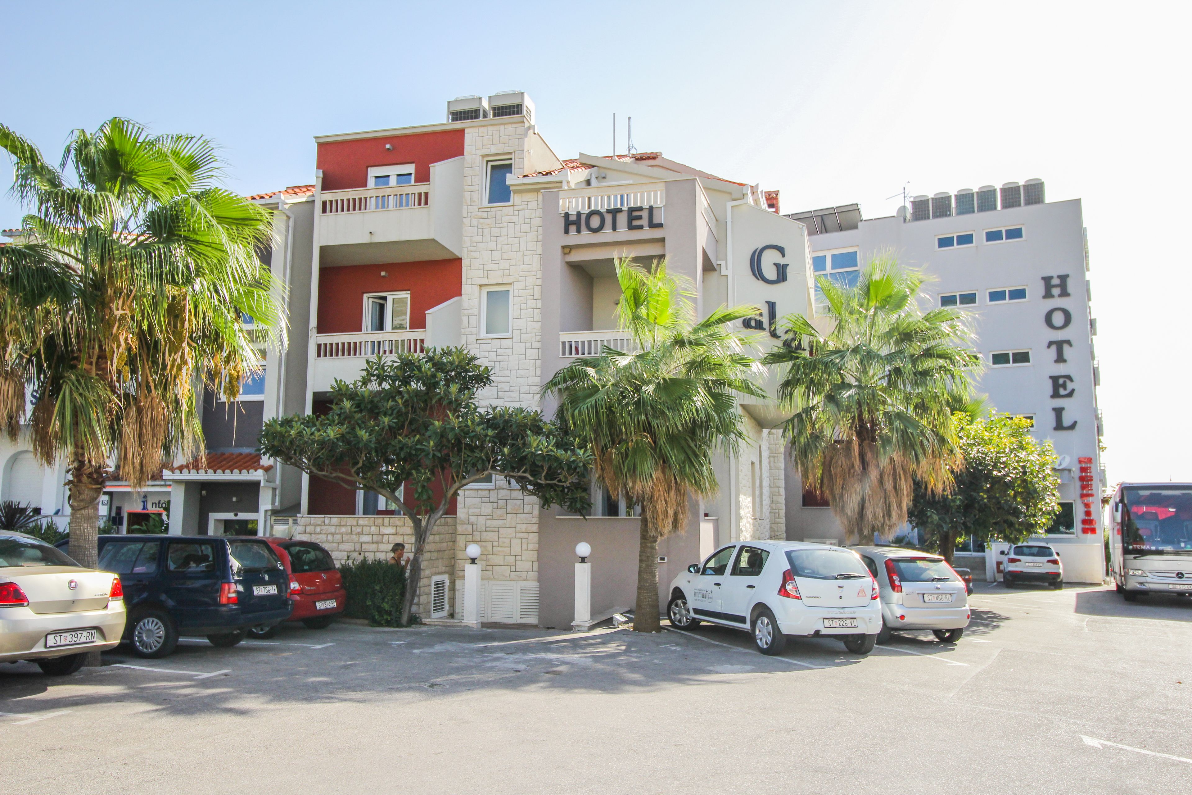 A hotel with a red and white facade, multiple balconies, and parked cars in the parking lot.