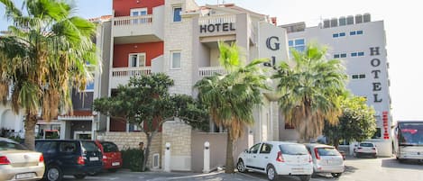 A hotel with a red and white facade, multiple balconies, and parked cars in the parking lot.