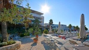 A resort pool area with sun loungers, umbrellas, and potted plants.