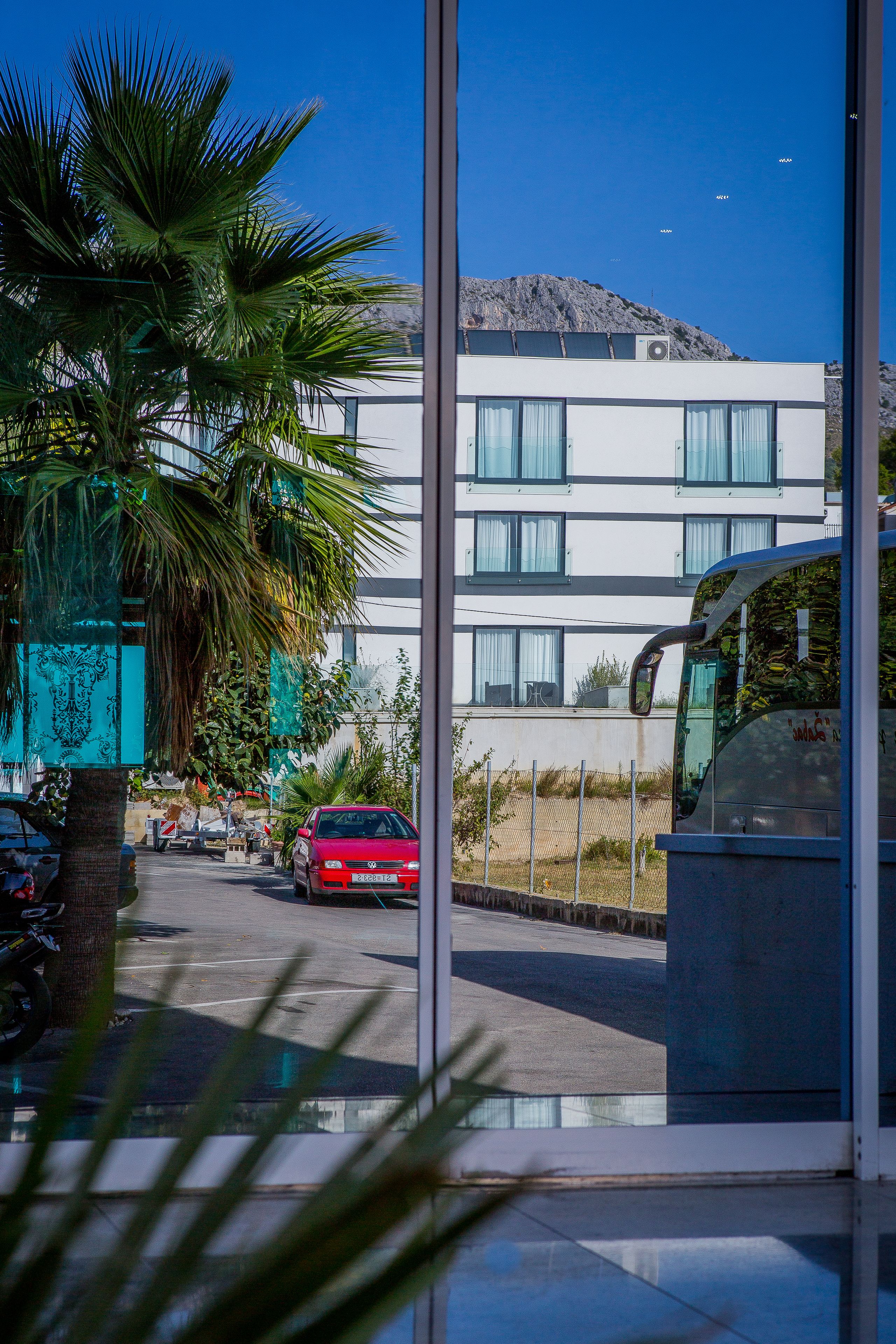 A modern building with a parking area, a red car, and a palm tree.