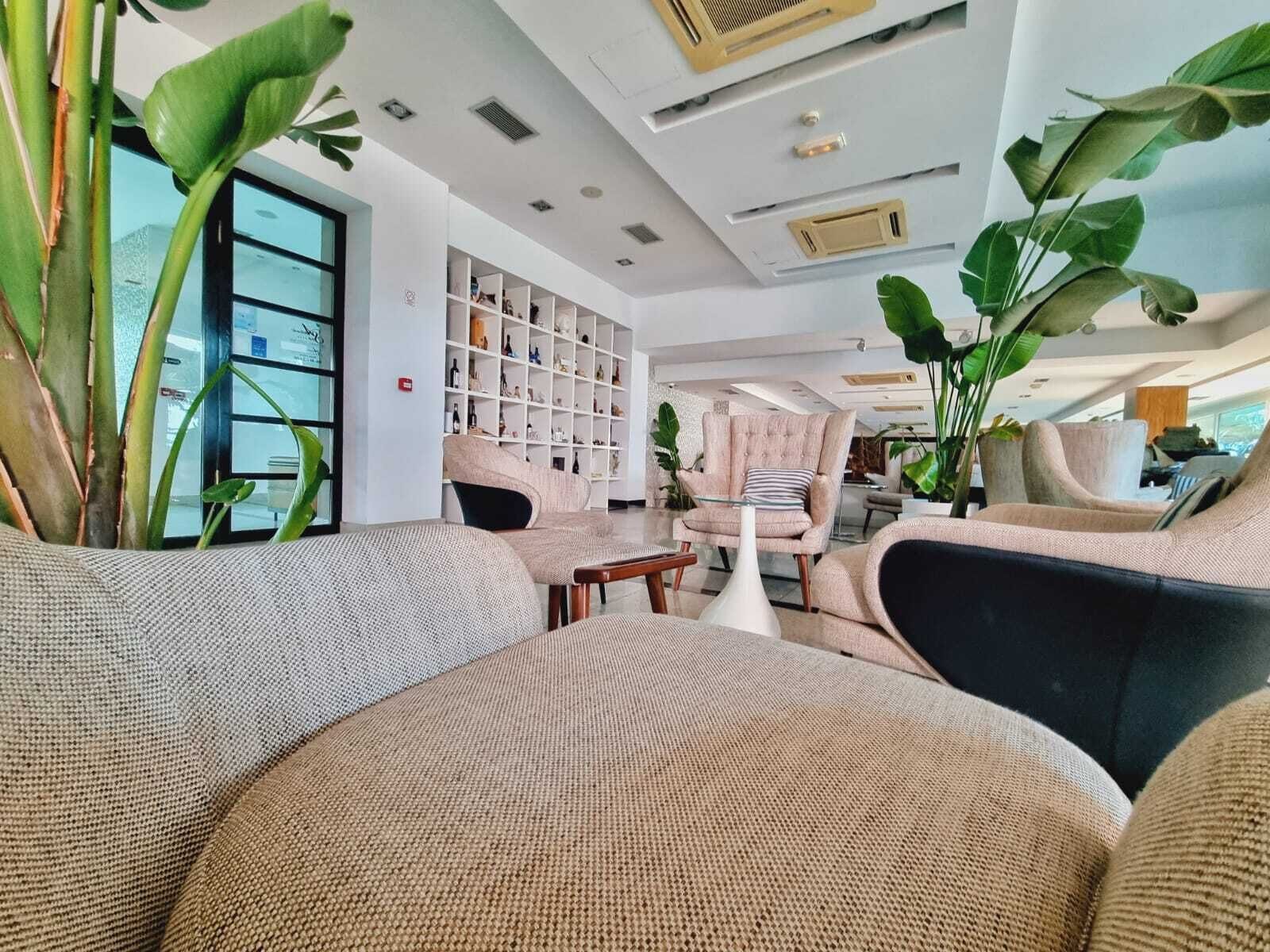 Una sala de estar moderna con un sofá, sillones y una mesa de centro. Se observa una estantería llena de libros y objetos decorativos.