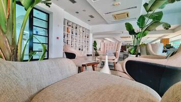 Una sala de estar moderna con un sofá, sillones y una mesa de centro. Se observa una estantería llena de libros y objetos decorativos.