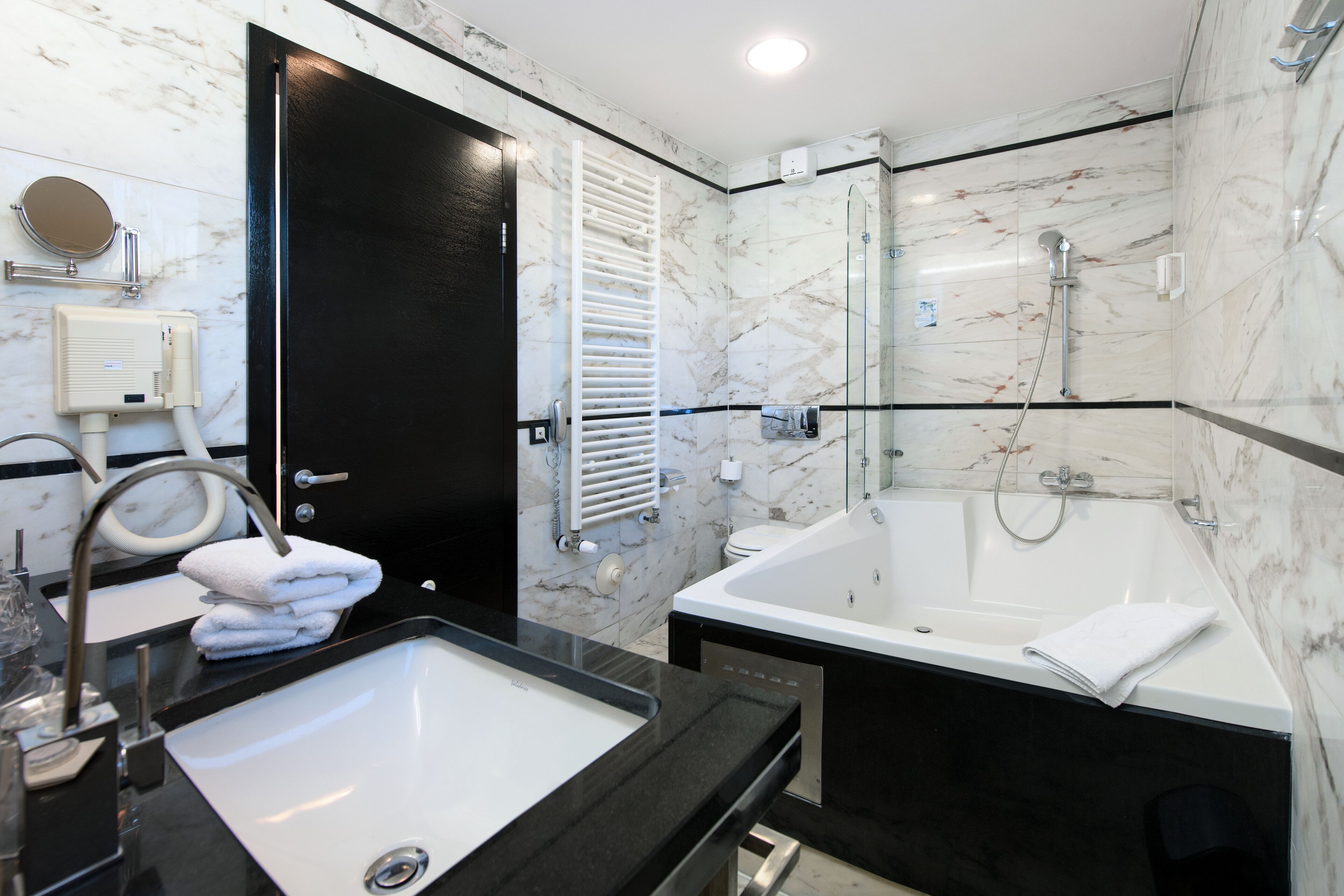 A modern bathroom with a black and white marble design, featuring a sink, a large bathtub, and a glass-enclosed shower area.
