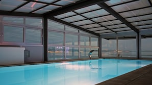 An indoor swimming pool with a view of a cityscape through large windows. - Hotel San Antonio (Podstrana)
