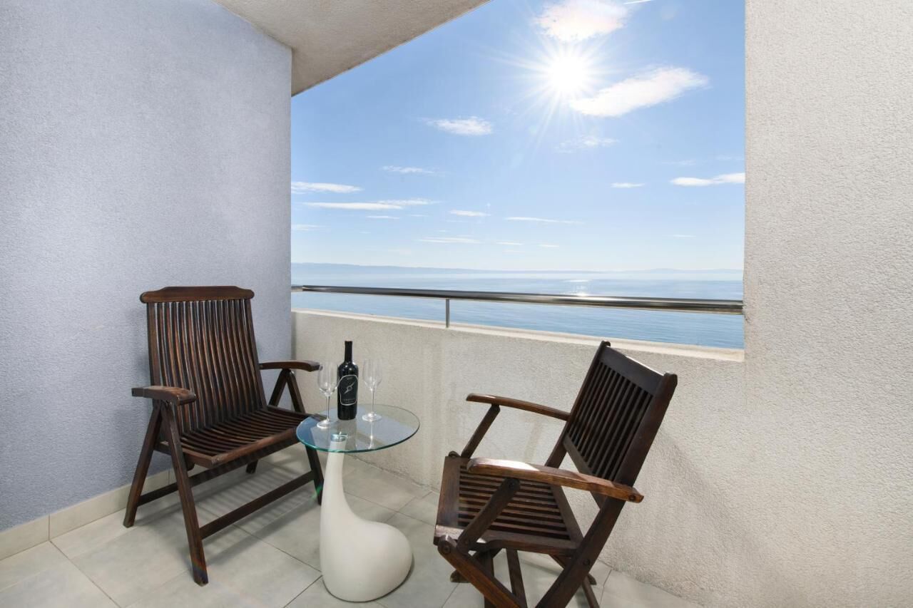 Un balcon avec deux chaises en bois et une table en verre, une bouteille et deux verres à vin.