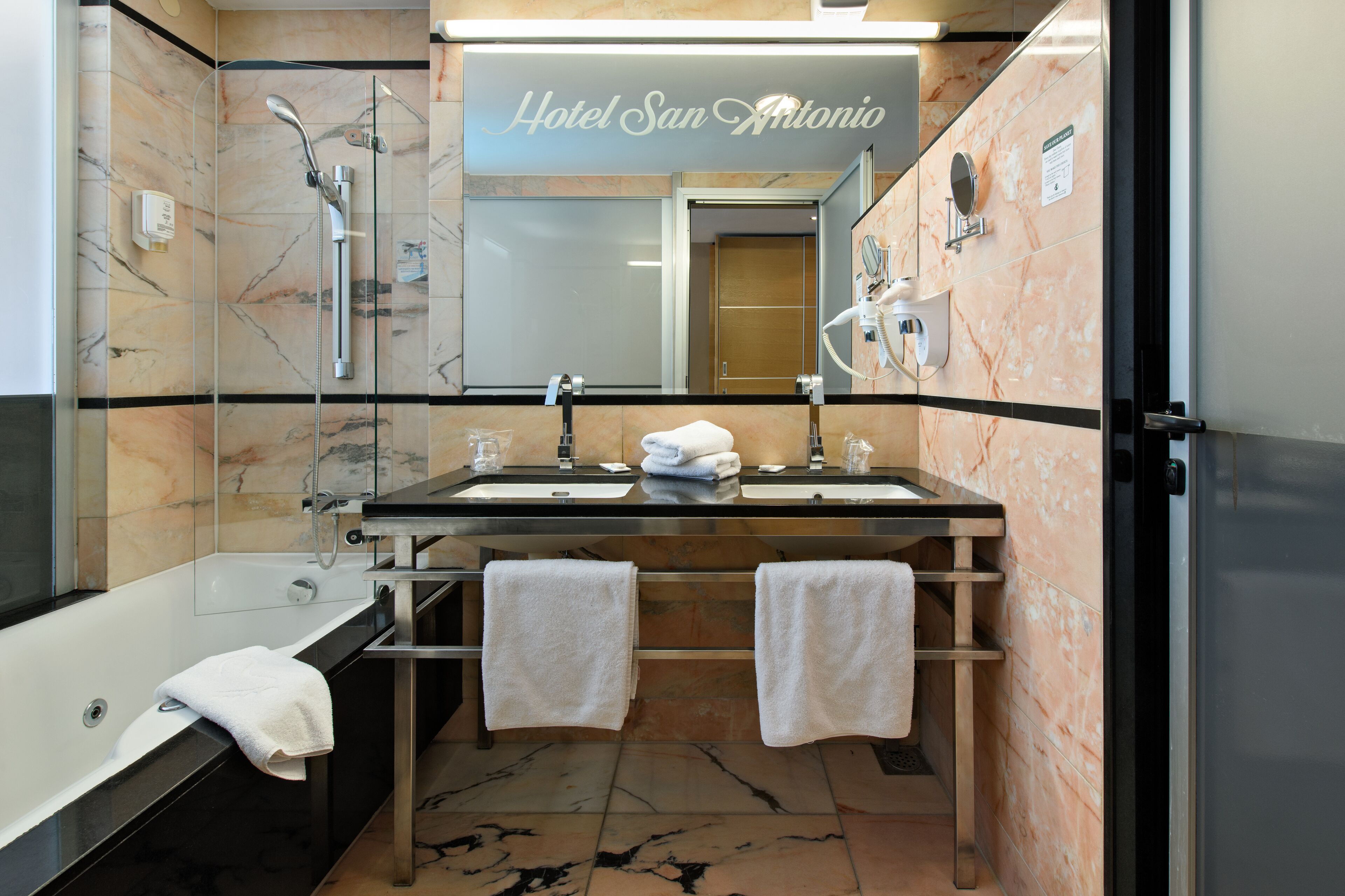 Ein modernes Badezimmer mit zwei Waschbecken, einer Badewanne und einer Dusche. Handtücher hängen an einem Halter, und die Wände sind mit einem Marmormuster verziert.