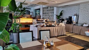 A modern hotel dining area with a buffet setup, a seating area with tables and chairs, and a patterned wall in the background.