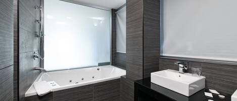 A modern bathroom with a large bathtub, a sink, and a mirror.
