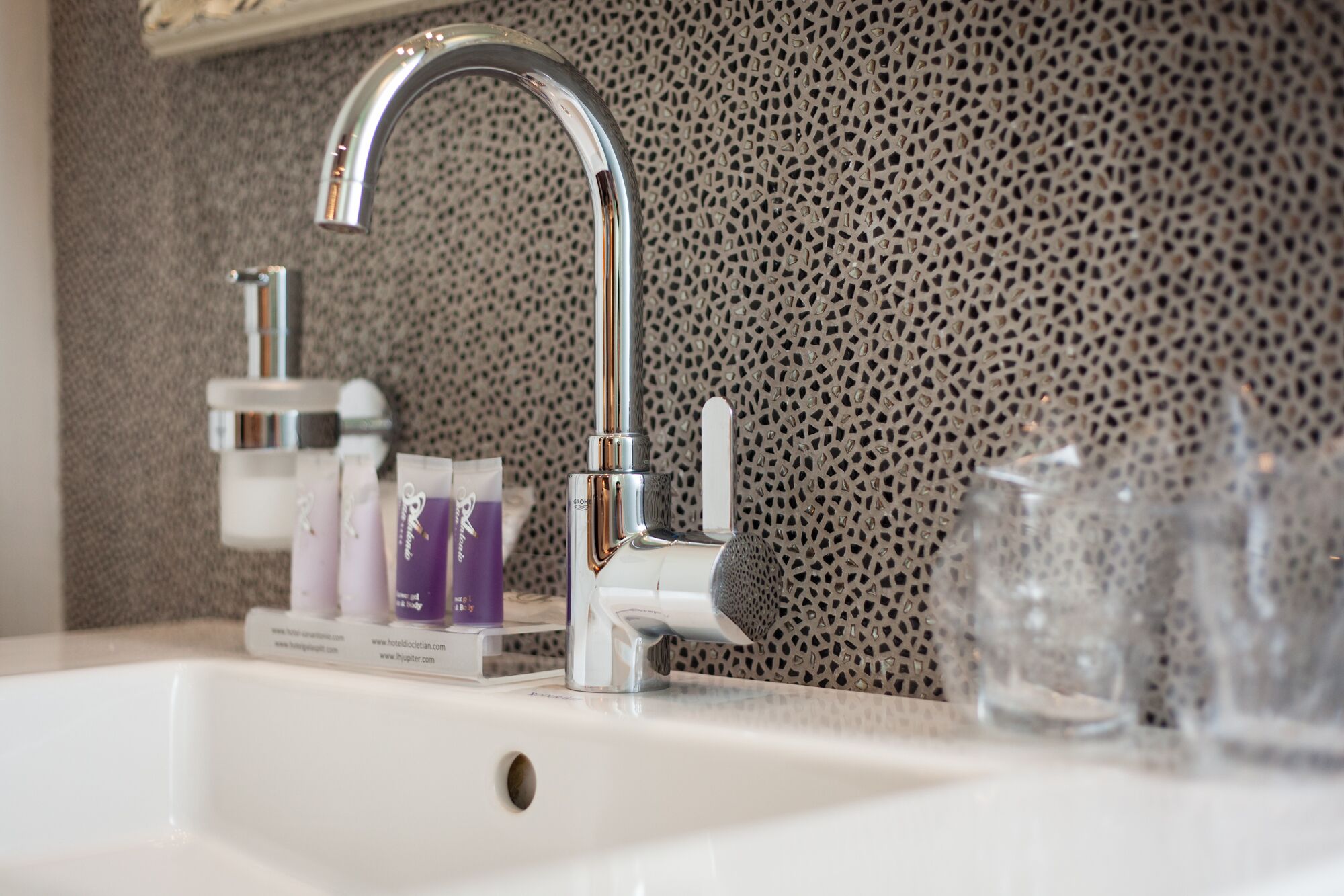 A modern bathroom sink with a chrome faucet, a textured wall, and toiletries on the counter.