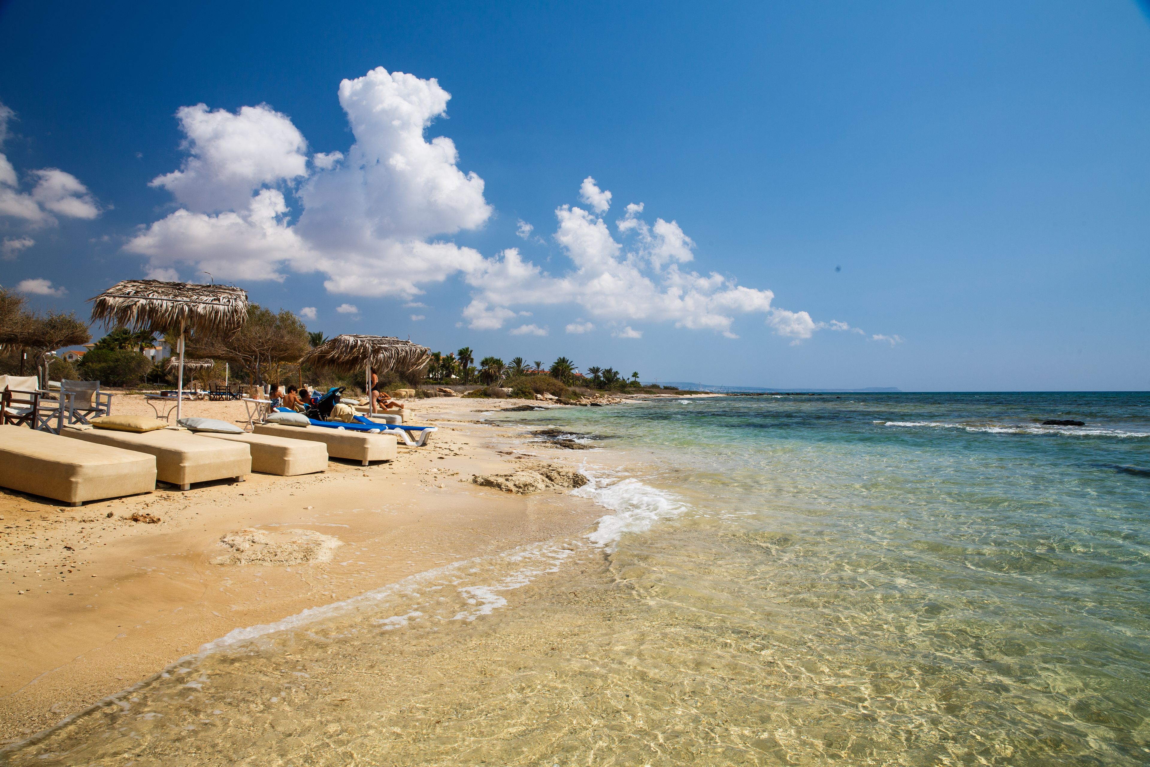 A beach with clear water, lounge chairs, and a thatched umbrella.