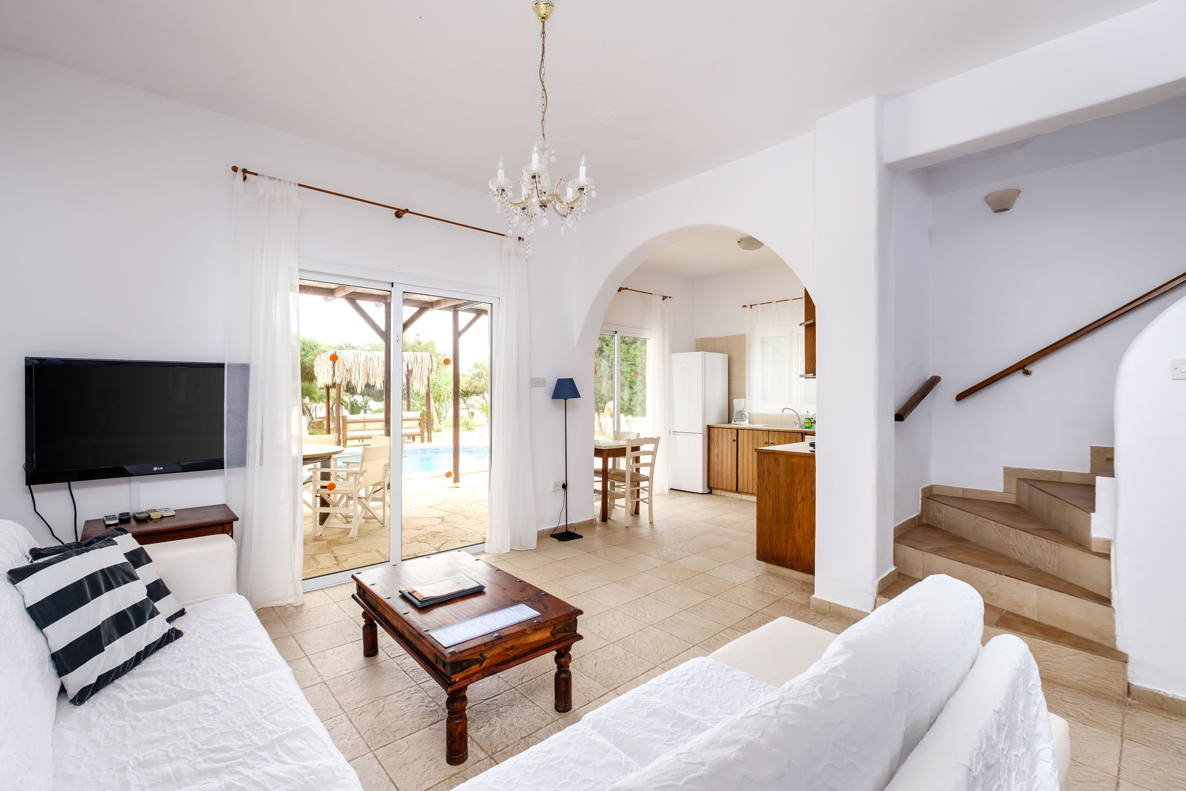 A spacious living room with a large TV, a sofa, a coffee table, and a view of an outdoor patio area.