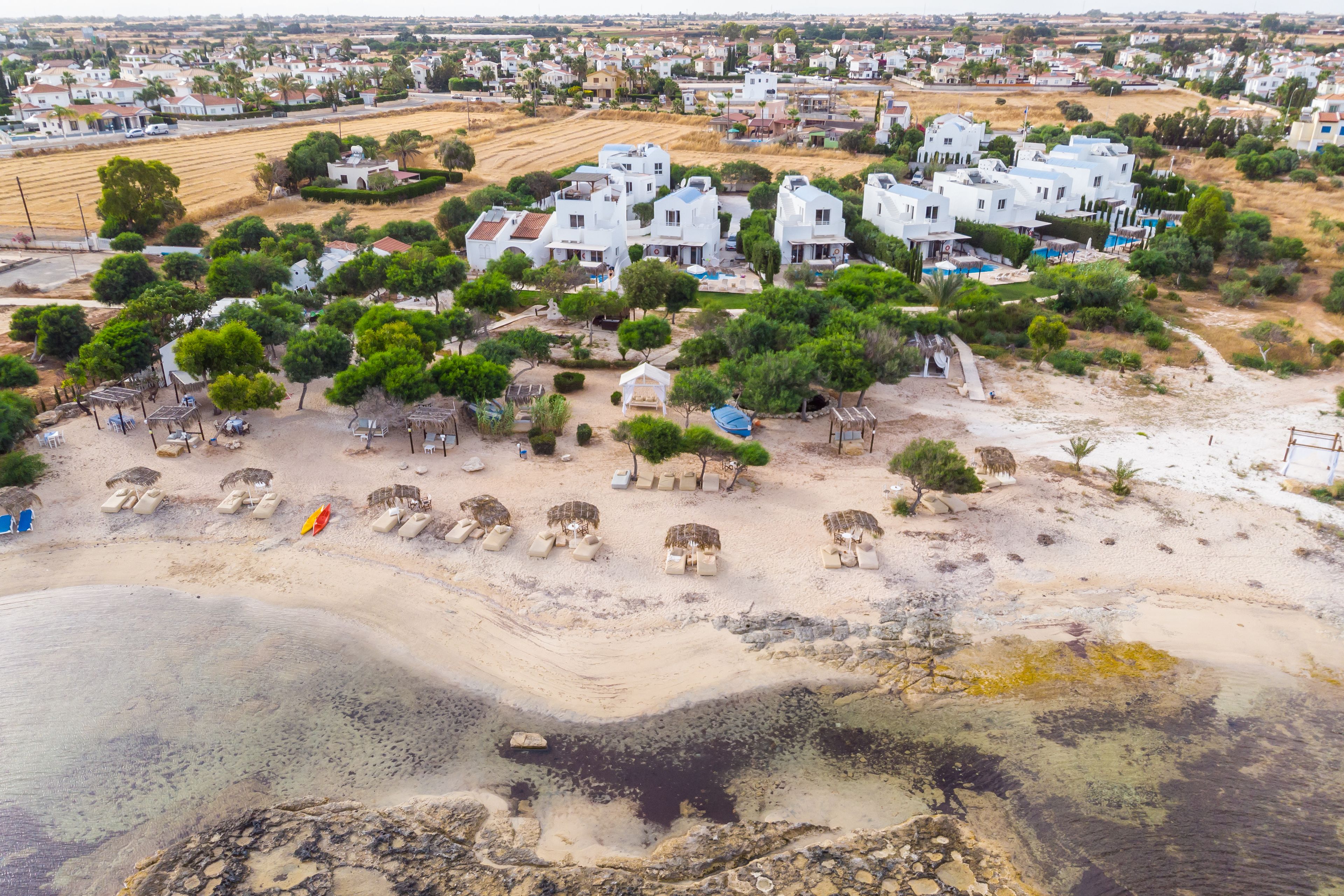 Vista aérea de una zona costera con edificios blancos, una playa de arena y una pequeña masa de agua.