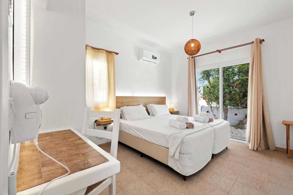 Un dormitorio moderno con una cama, mesitas de noche, una silla de masaje y vistas al exterior.