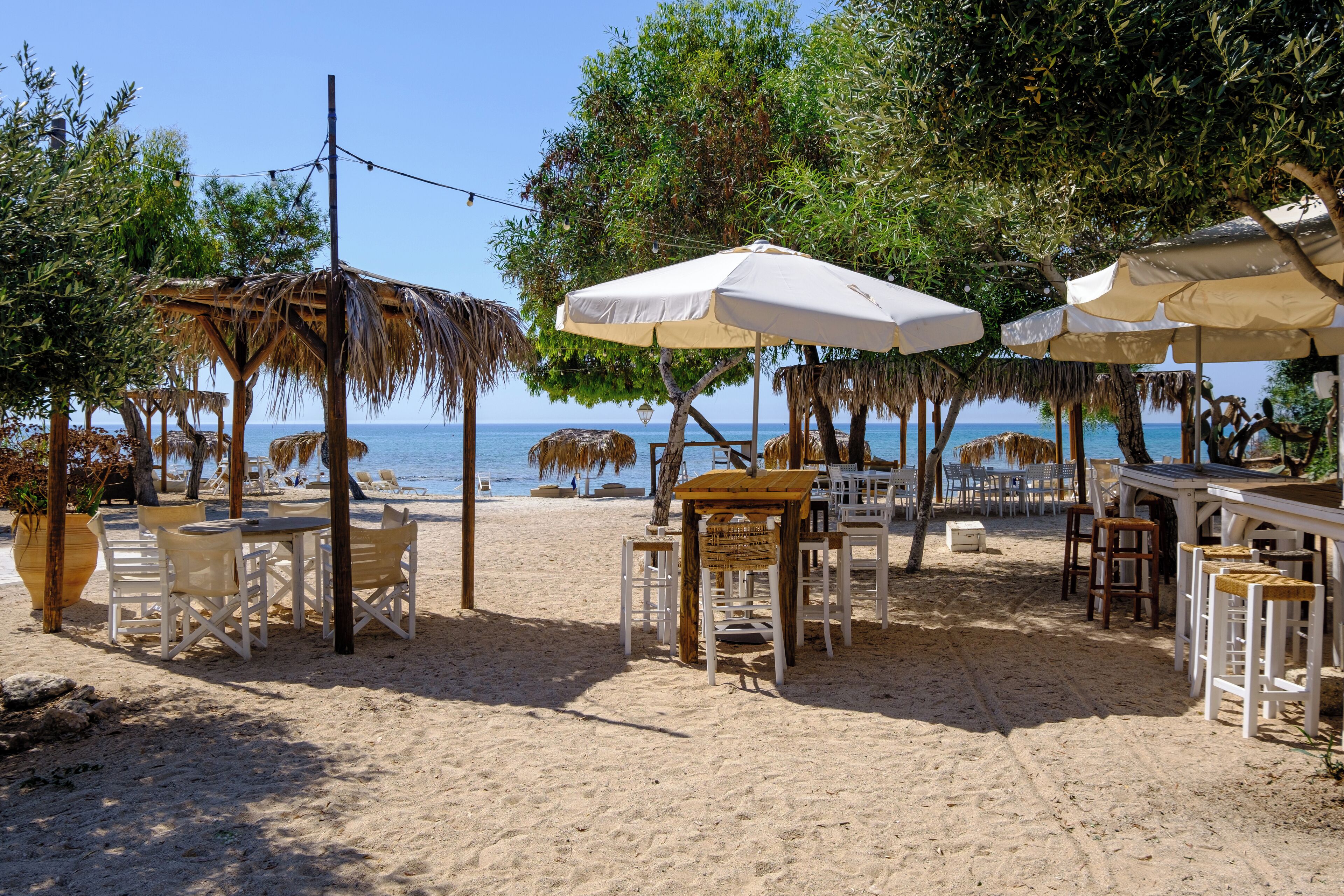 A beachside restaurant with outdoor seating, including tables and chairs, under umbrellas.
