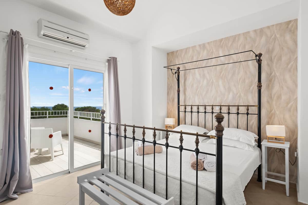 A bedroom with a four-poster bed, a balcony with white chairs, and a view of the sky.