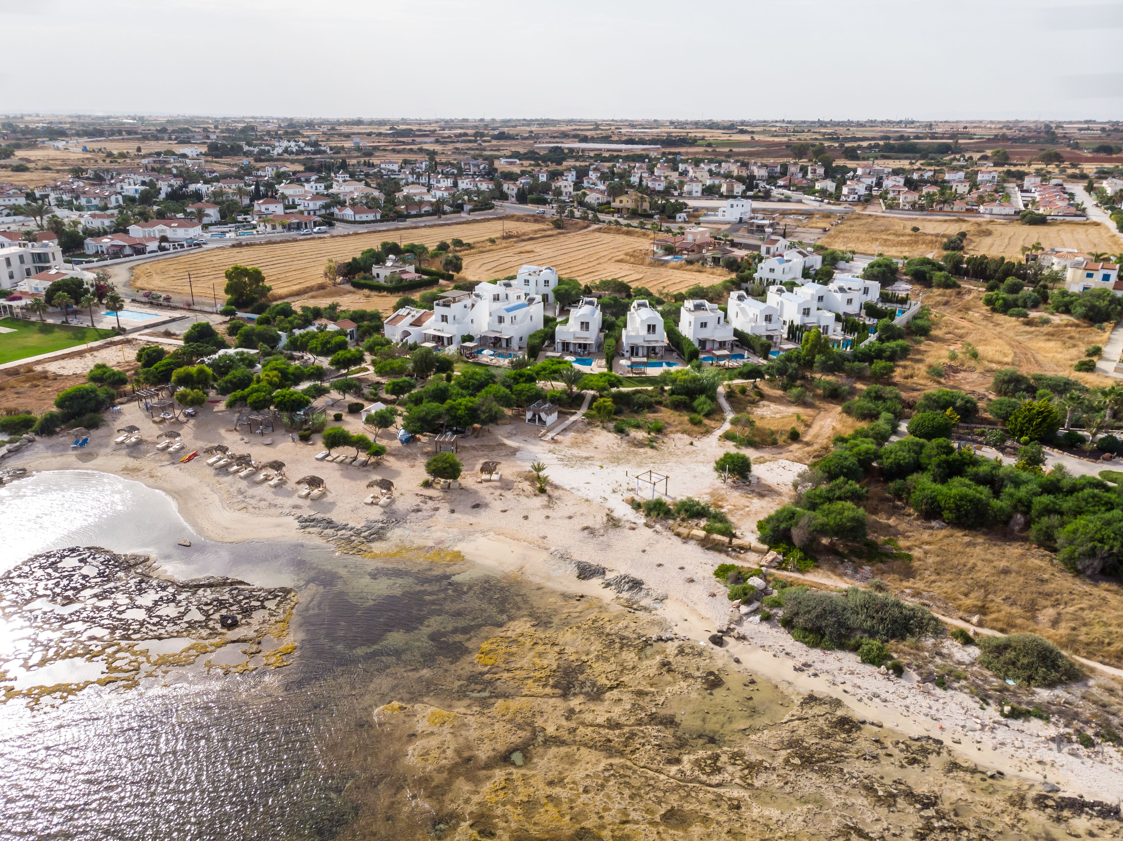 Um resort costeiro com vários edifícios brancos, uma praia arenosa e vista clara do mar.