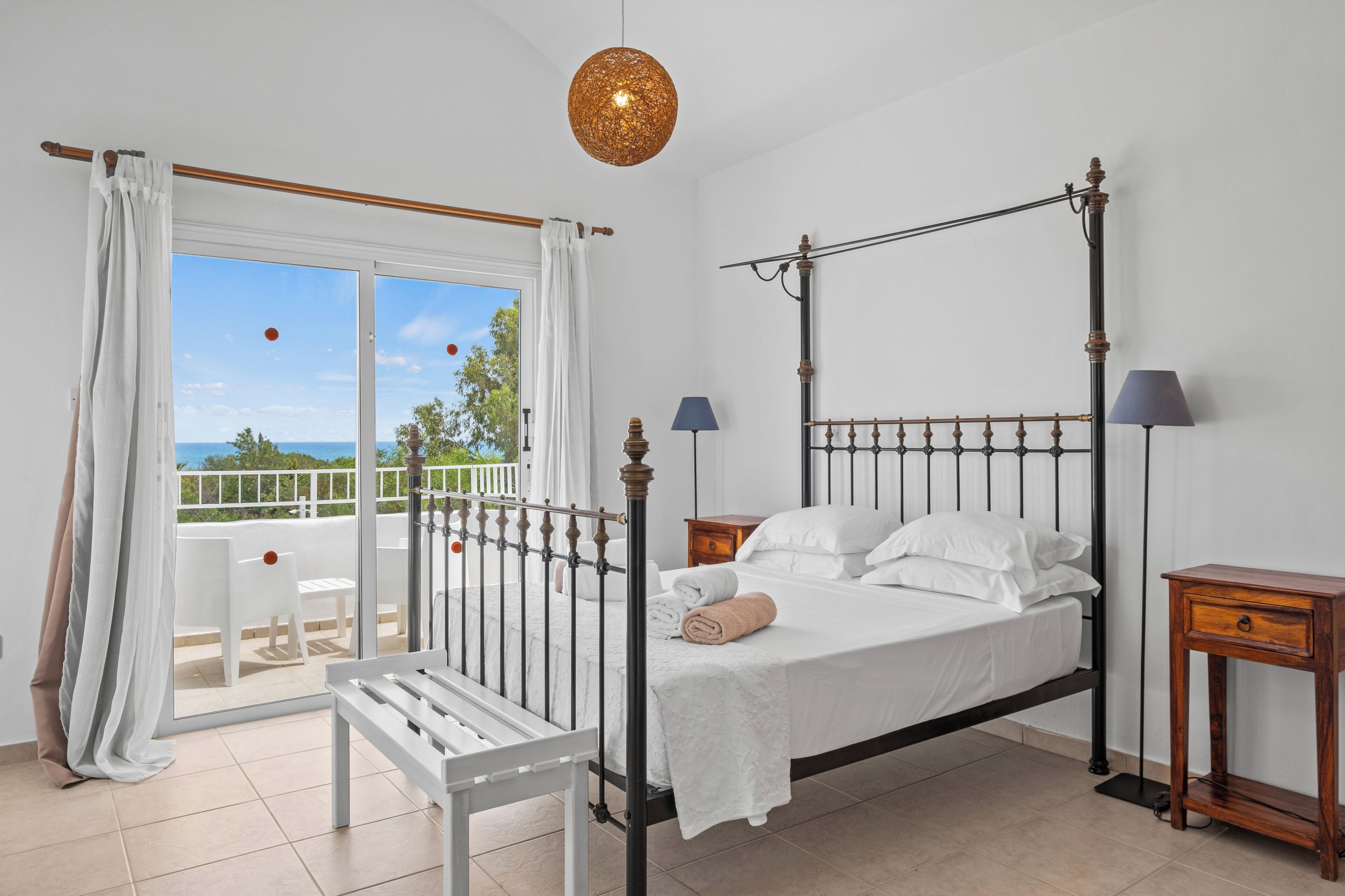 Un dormitorio con cama con dosel, un balcón con una silla blanca y vista al mar.