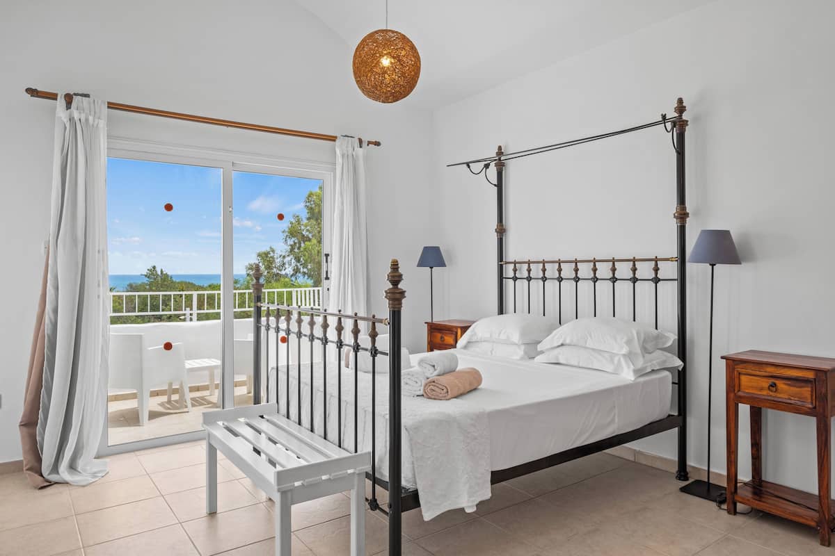Un dormitorio con cama con dosel, un balcón con una silla blanca y vista al mar.