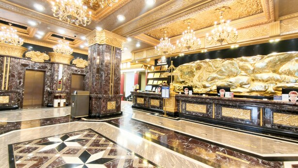 Un vestíbulo lujoso con pisos de mármol, candelabros ornamentales y una mesa de recepción.
