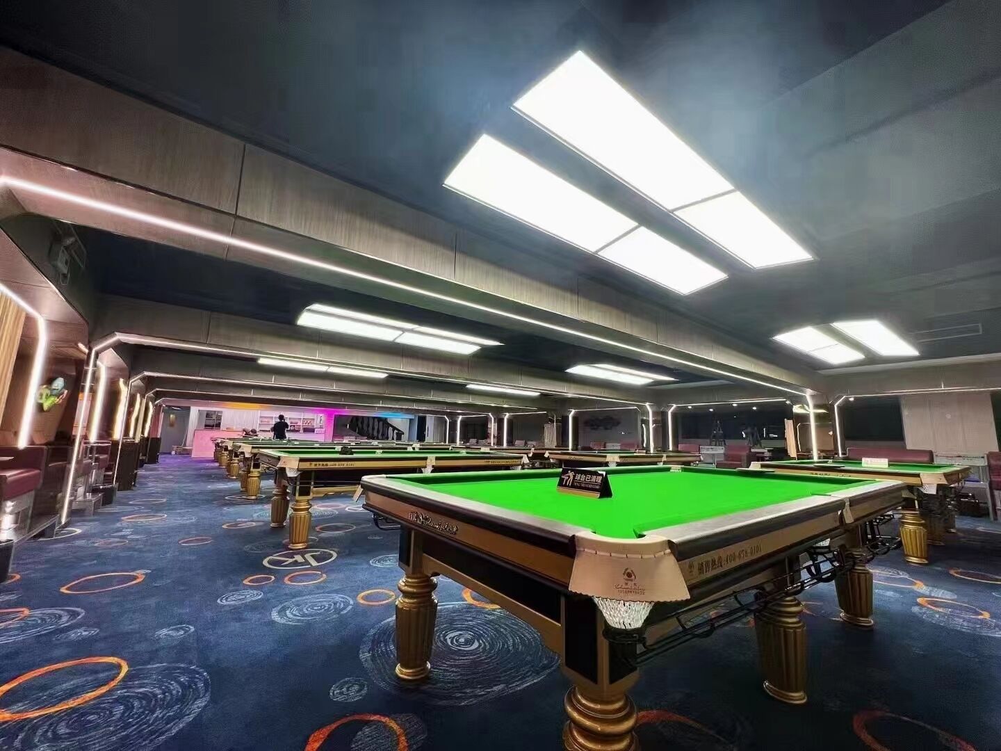 A pool hall with multiple tables and overhead lighting.