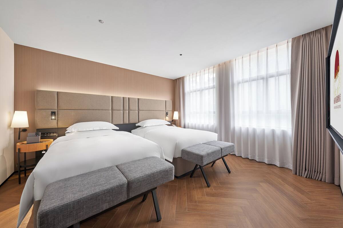 Habitación de hotel con dos camas, un escritorio y un ventanal con cortinas.