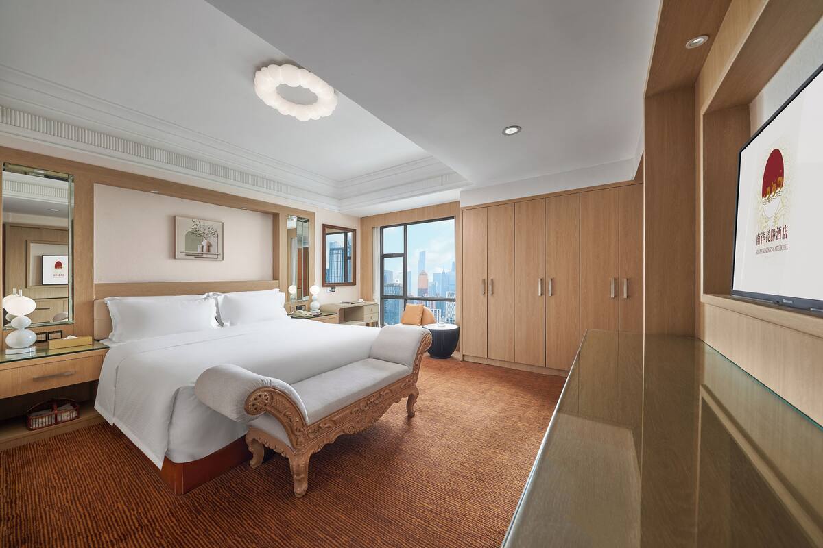 Habitación de hotel con una cama grande, un armario de madera, una mesa de vidrio y vistas a la ciudad.