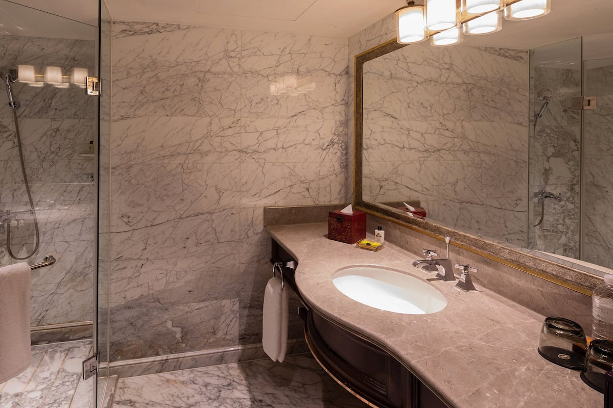 A modern bathroom with a glass-enclosed shower, a marble-tiled wall, a sink with a mirror, and a vanity with toiletries.