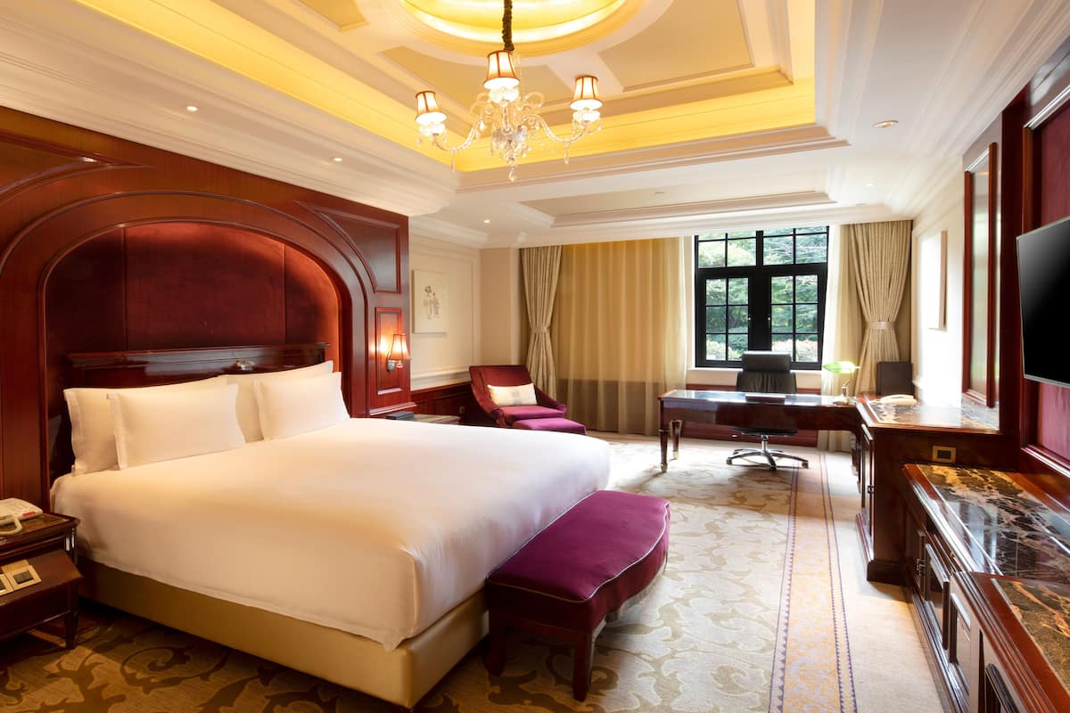 A spacious hotel room with a large bed, a desk, a chair, a television, and a window with curtains.