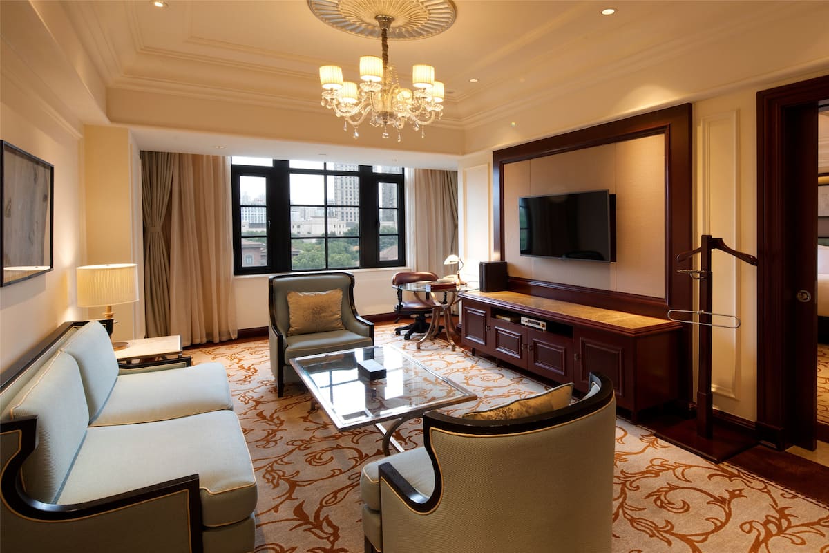 A hotel room with a sofa, armchair, a small table, a TV, a desk, and a bed.