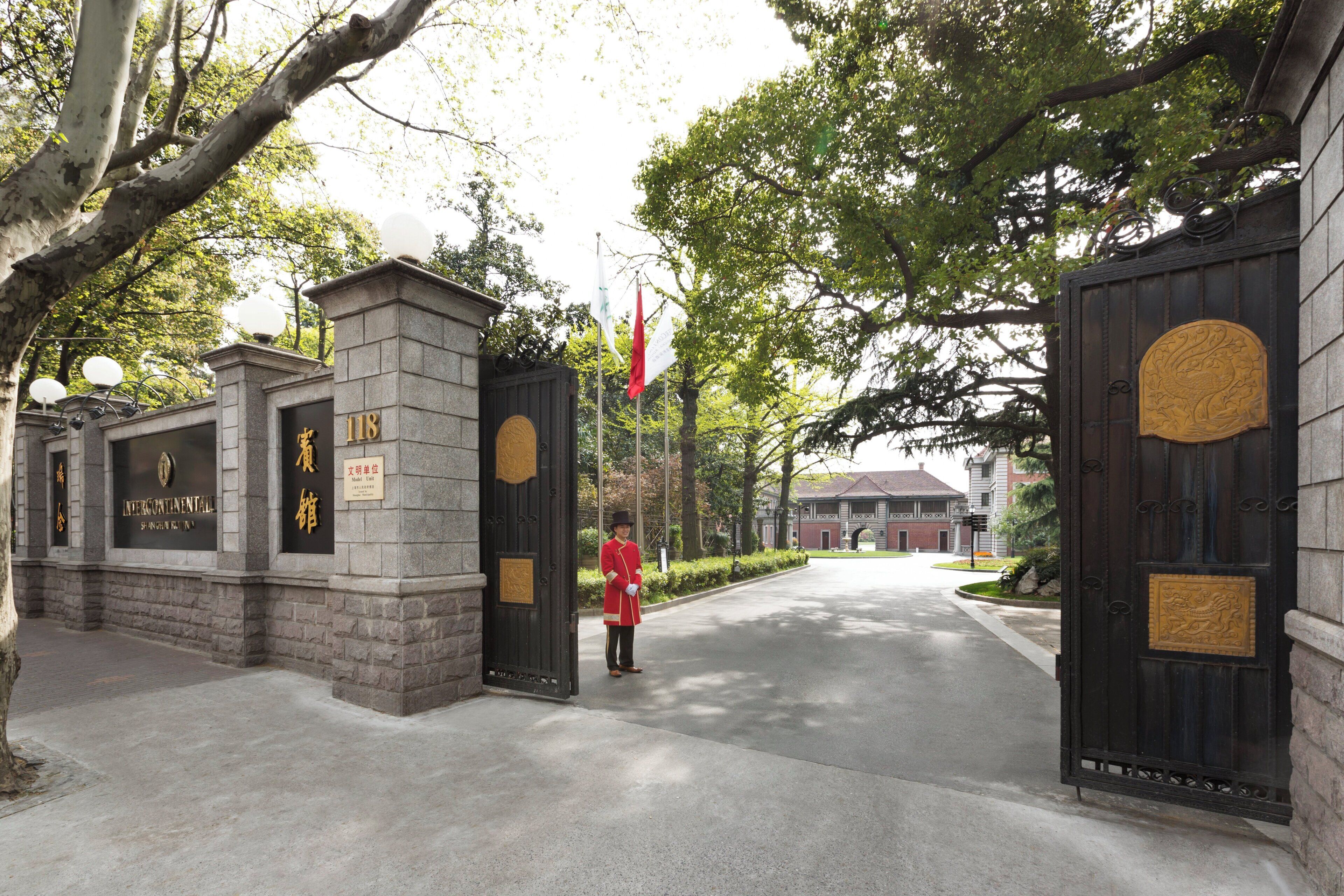 A gated entrance with stone pillars, a sign with Chinese characters, and a flag.