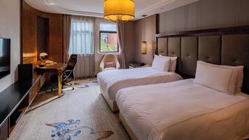 A hotel room with two beds, a desk with a chair, a television, and a large window.